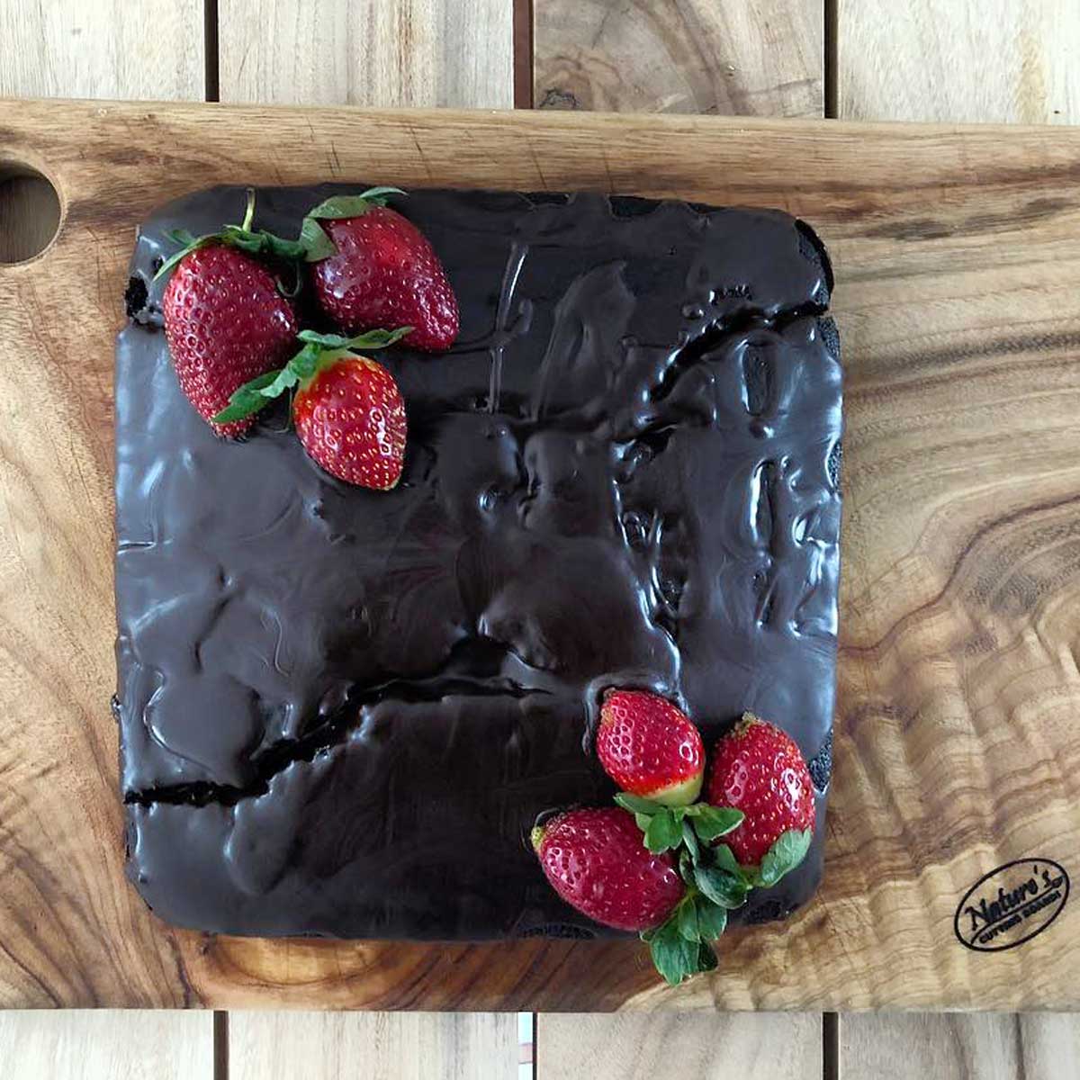 A stunning rectangular wood cutting and chopping board from Nature's Boards, designed with a round hole in one corner and decadent chocolate cake garnished with strawberries..